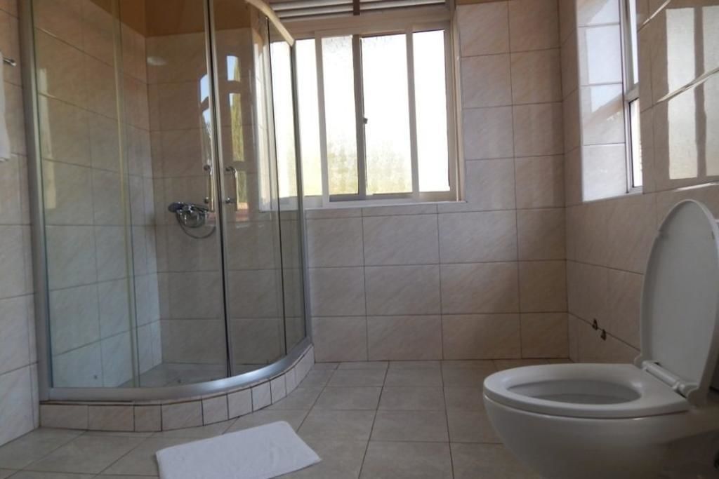 A bathroom with a glass shower enclosure, a toilet, and a window providing natural light.