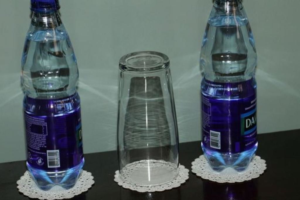 Tres botellas de plástico con etiquetas, un recipiente de vidrio vacío y un mantel individual sobre una mesa.
