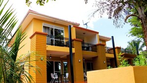 Un edificio de dos pisos con fachada amarilla, balcones y mesas al aire libre.