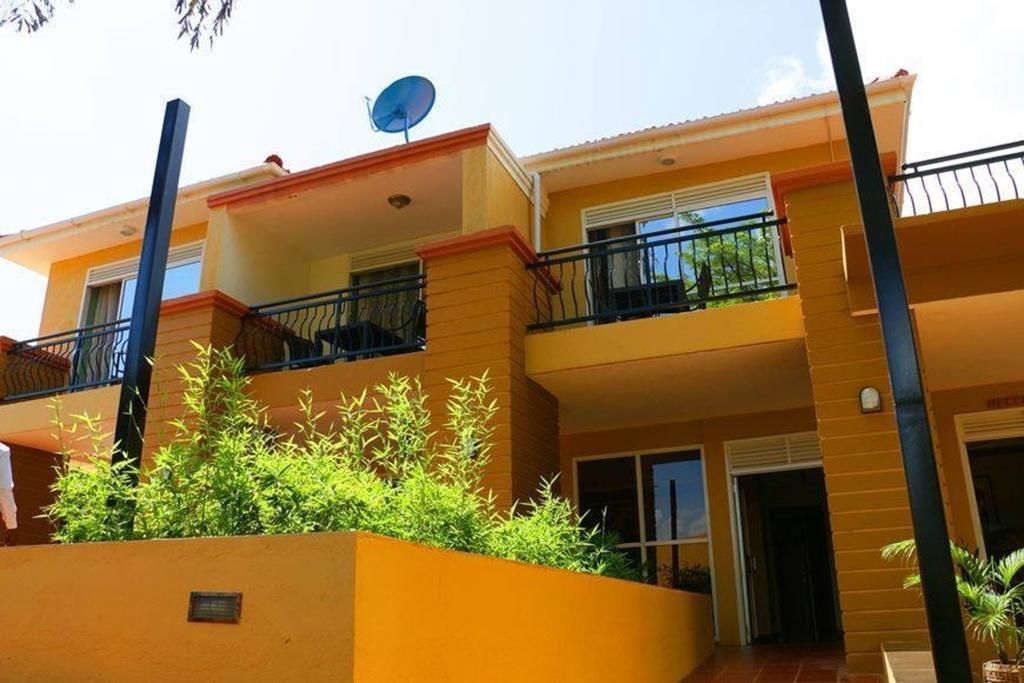 Un edificio residencial de varios pisos con balcones, antena parabólica y un pequeño jardín.