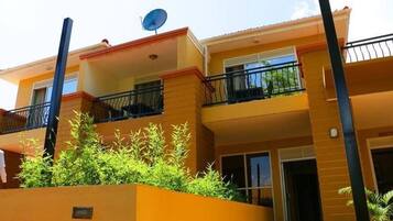 Un edificio residencial de varios pisos con balcones, antena parabólica y un pequeño jardín.