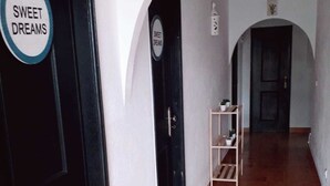 A hallway with a sign reading "SWEET DREAMS" on a door, a tiled floor, and a small shelf with plants. - Backpackers Hostel Fonte da Telha (Almada)