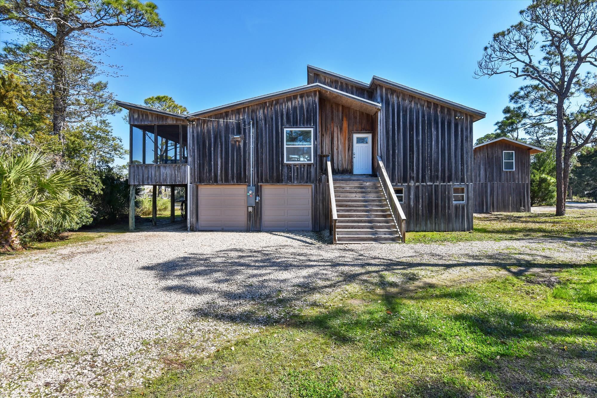A rustic wooden house with a front porch, a garage, and a staircase leading to the entrance.