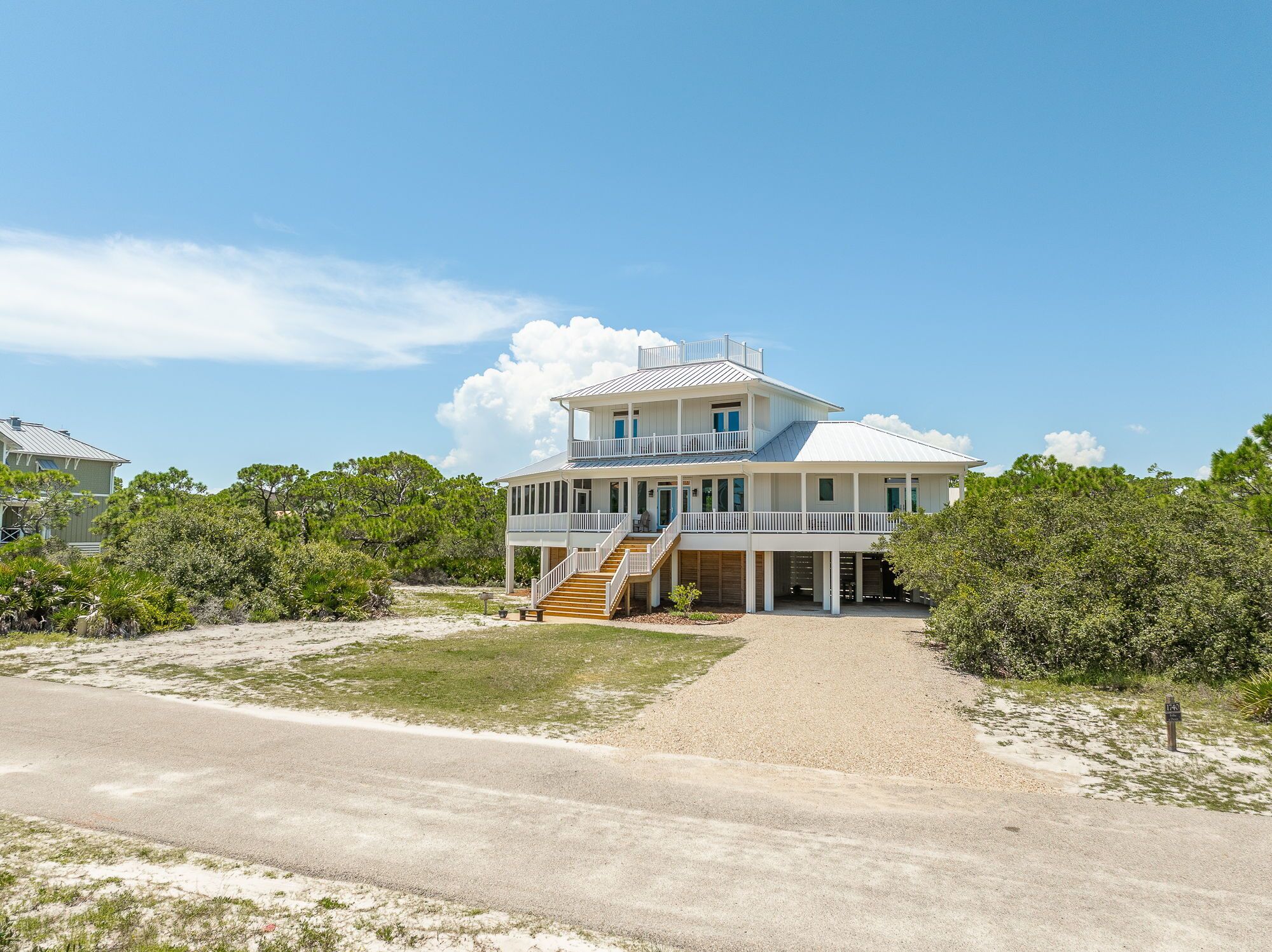 A two-story beachfront house with a covered porch and a staircase leading to the upper level.