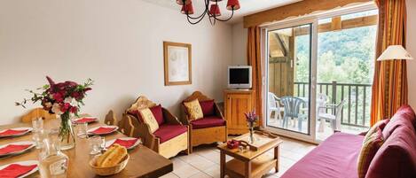 A cozy room with a wooden dining table set for four, a sofa, and a TV on a wooden cabinet.