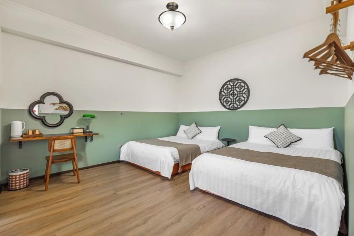 A hotel room with two beds, a wooden chair, a small table with a lamp, and a wall-mounted decorative item.