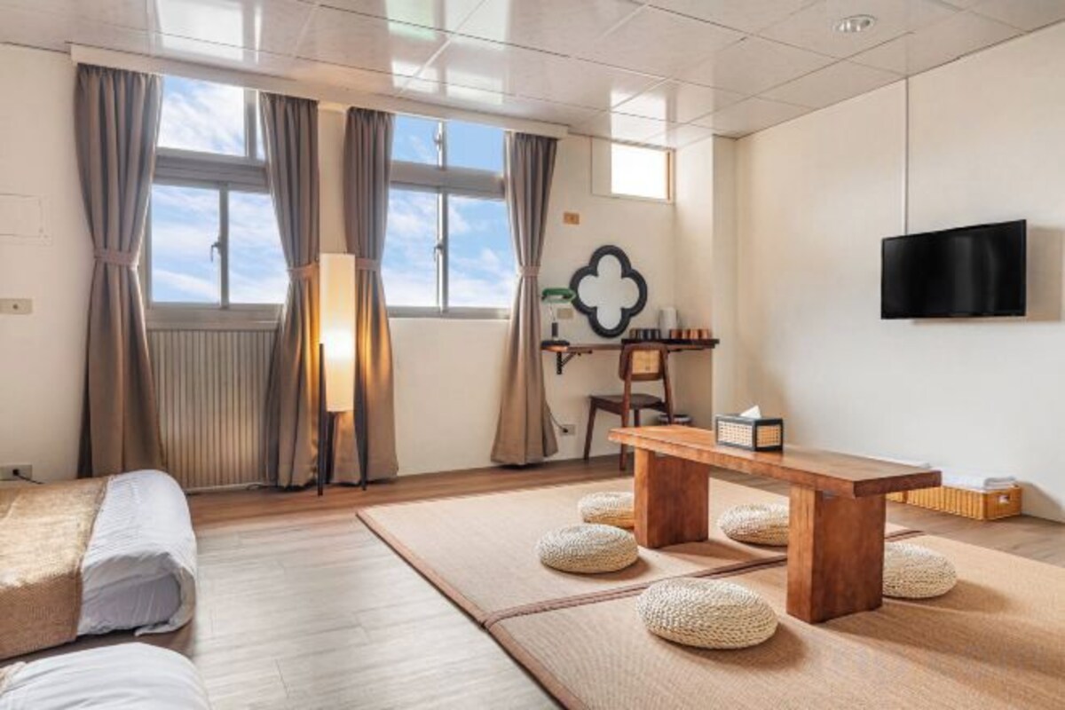A room with a bed, a wooden table, tatami mats, a TV, and a window with curtains.