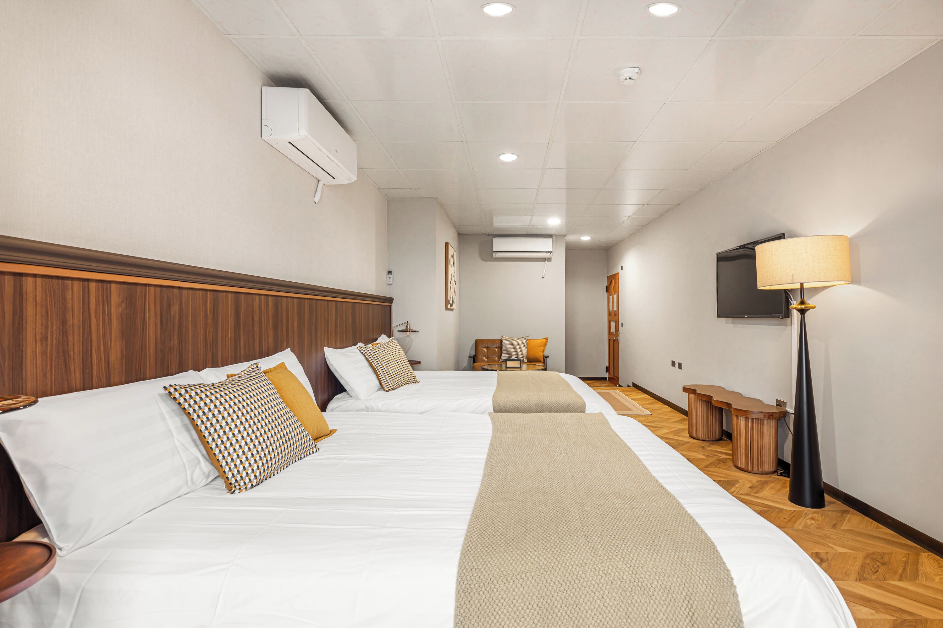 Una habitación de hotel con dos camas, televisión, lámpara y suelo de madera.