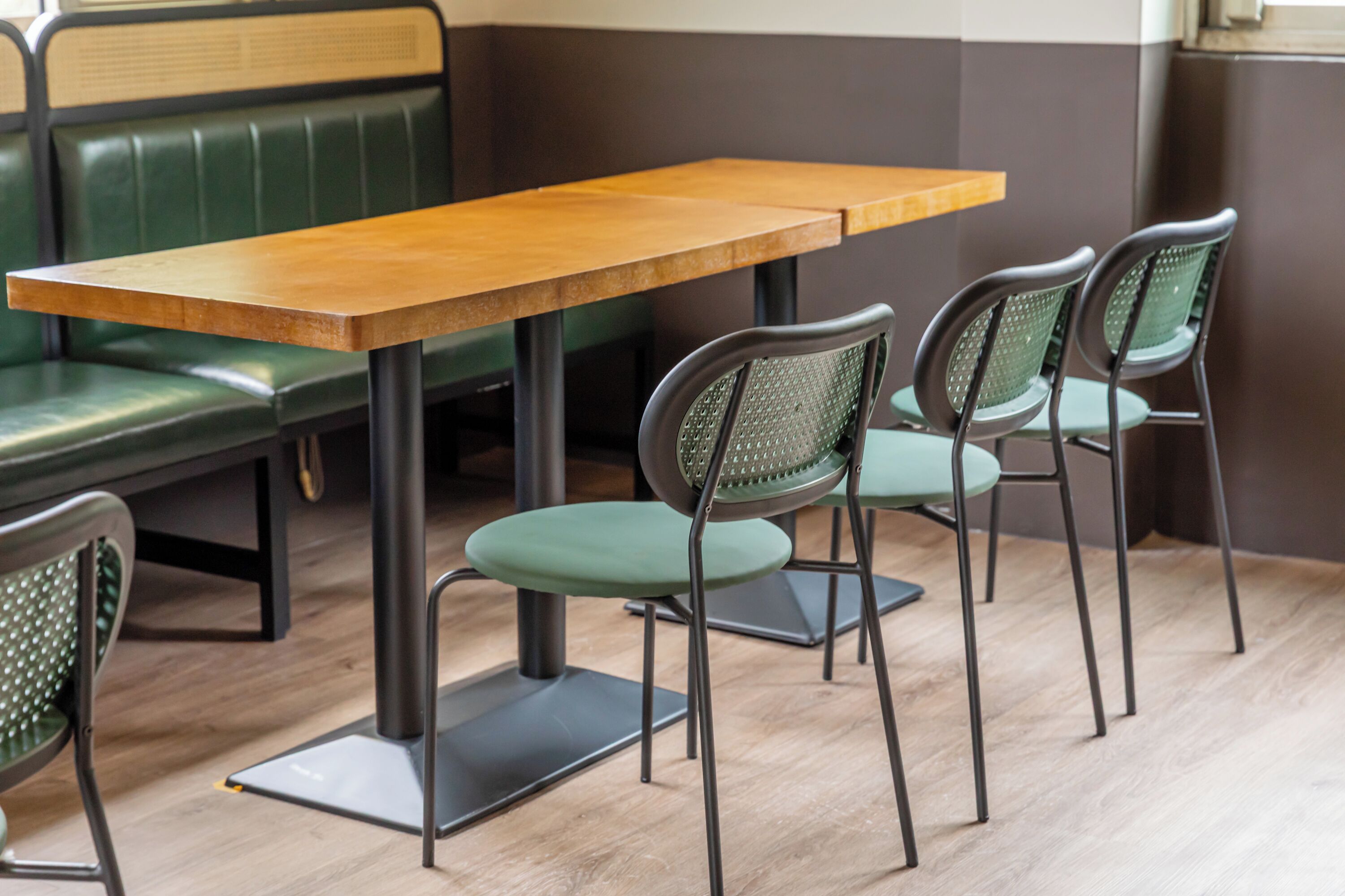 A dining area with a wooden table and four chairs with green cushions.