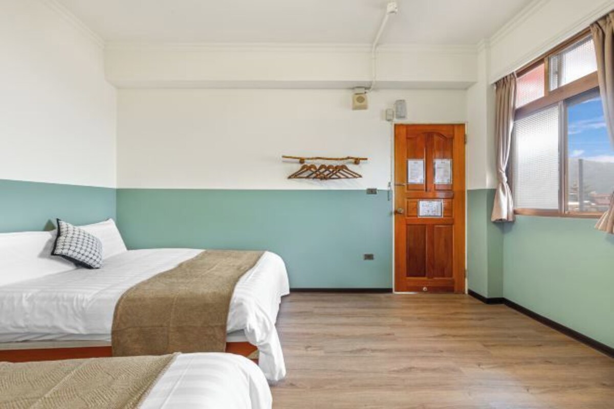 A hotel room with two beds, a wooden door, and a window with curtains.