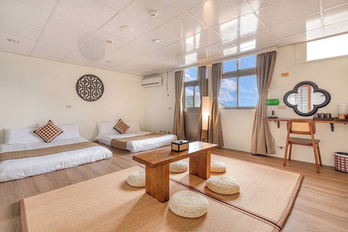 Et moderne hotelværelse med trægulv, en stor seng, to mindre senge, et træbord og et spejl på væggen.