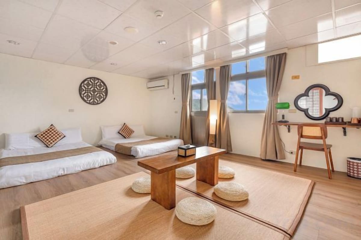 Une chambre d’hôtel avec deux lits, une table en bois et une vue sur le ciel par de grandes fenêtres.