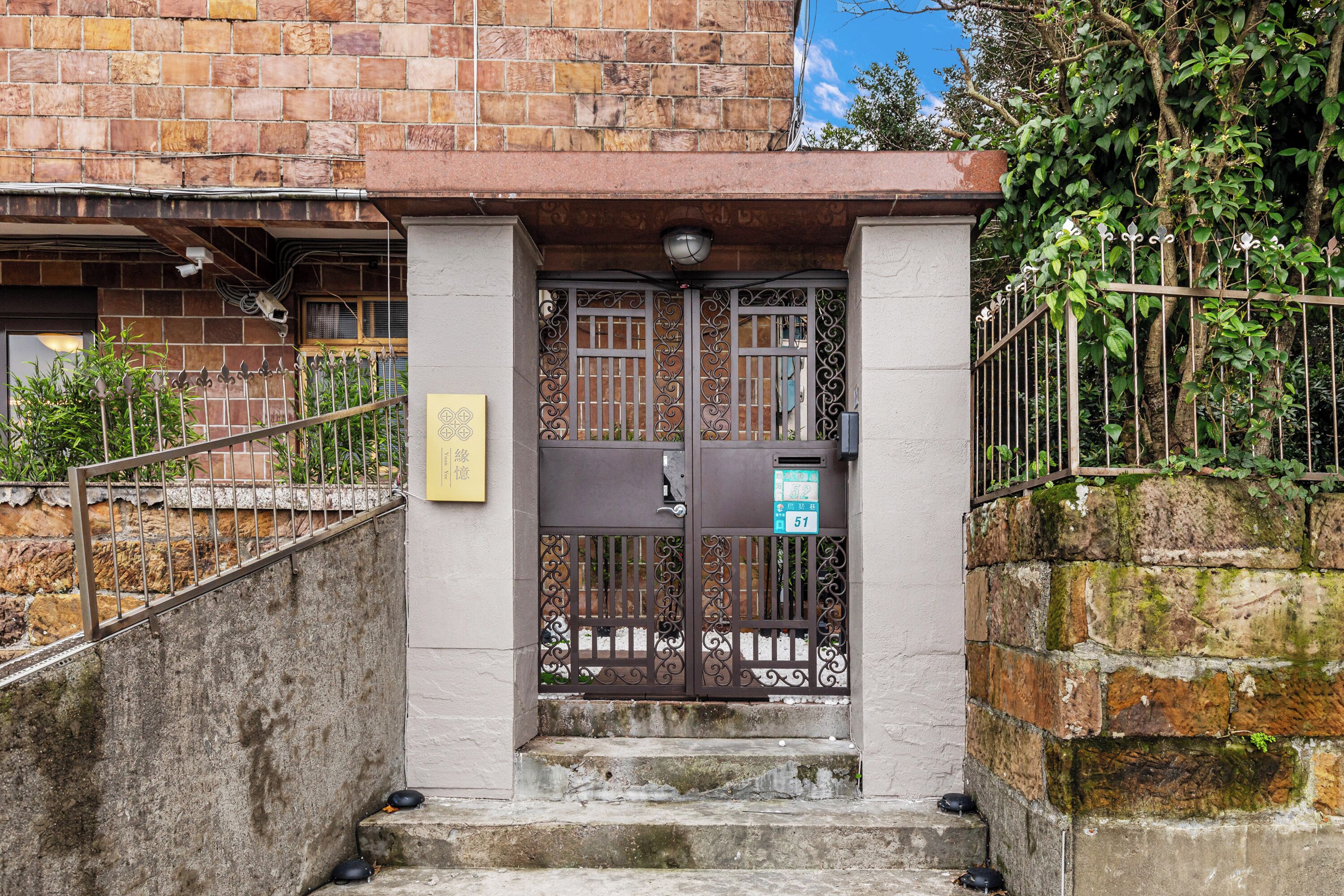 A gated entrance with a metal gate, steps leading up to a building with a stone facade, and a sign on the wall.