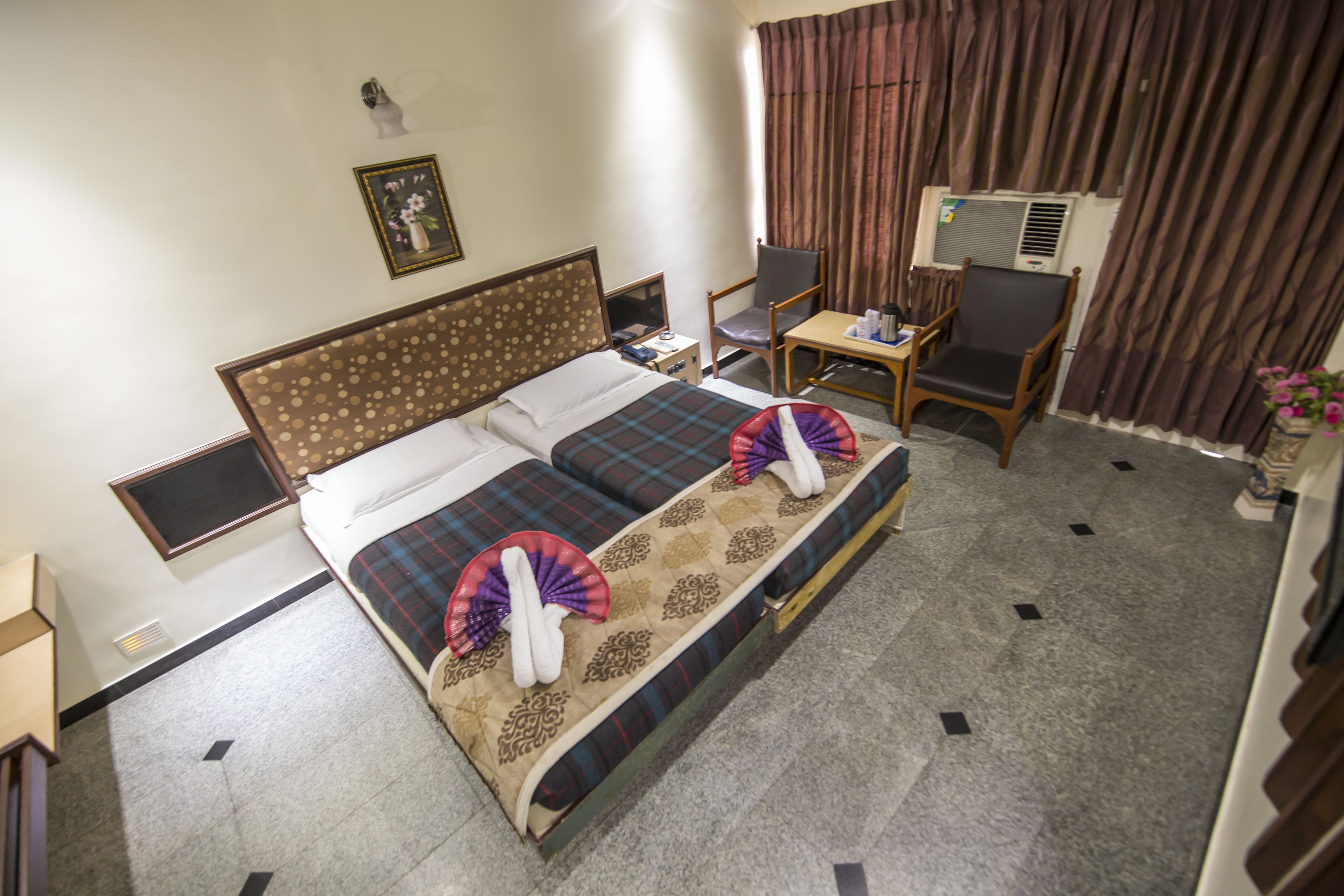 A hotel room with a bed, a desk, a chair, an air conditioner, and a window with curtains.