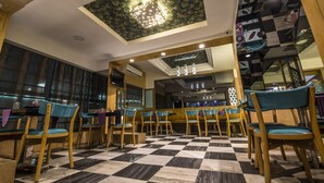 A restaurant interior with checkered flooring, wooden chairs, and a central light fixture. - Hotel Aryaas (Tirunelveli)