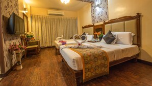 A hotel room with a wooden bed, a television, a desk with a chair, and a bathroom with a shower curtain. - Hotel Aryaas (Tirunelveli)