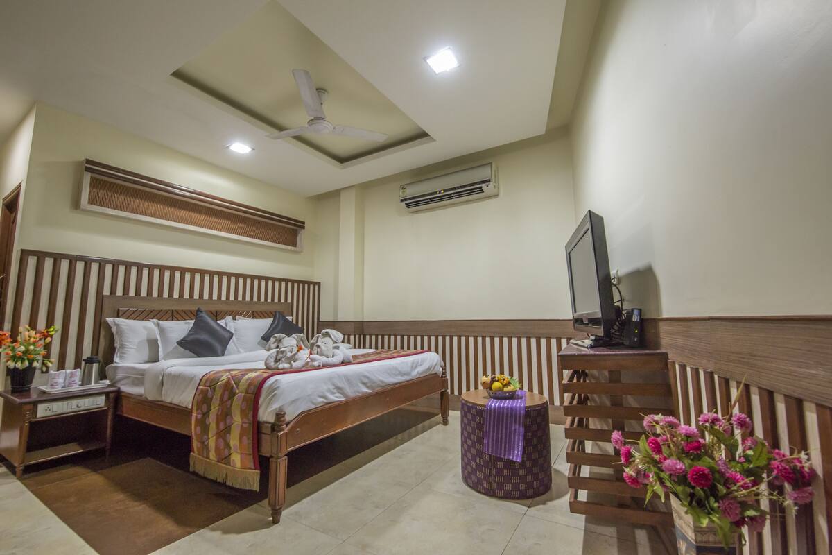A hotel room with a bed, bedside table, nightstand, TV, and a small table with flowers.
