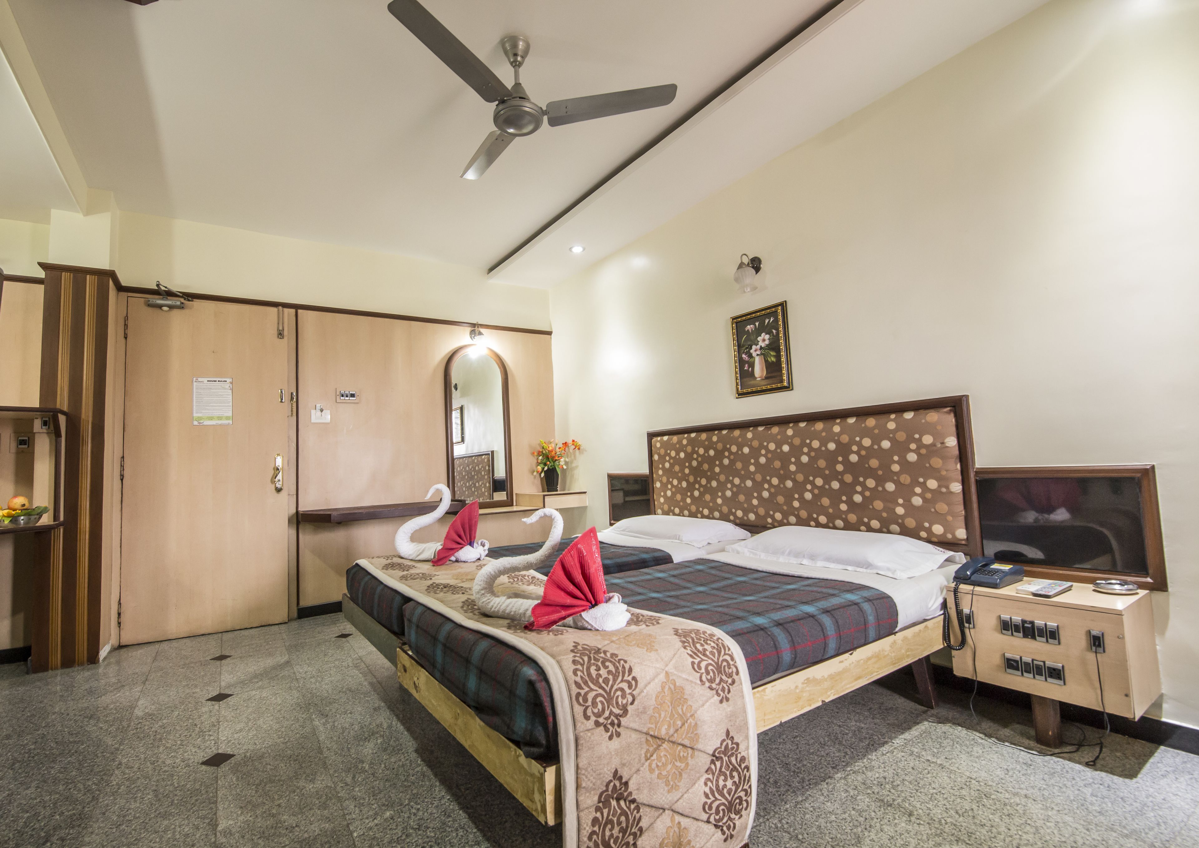 A hotel room with a bed, a ceiling fan, a bedside table with a phone, and a mirror.