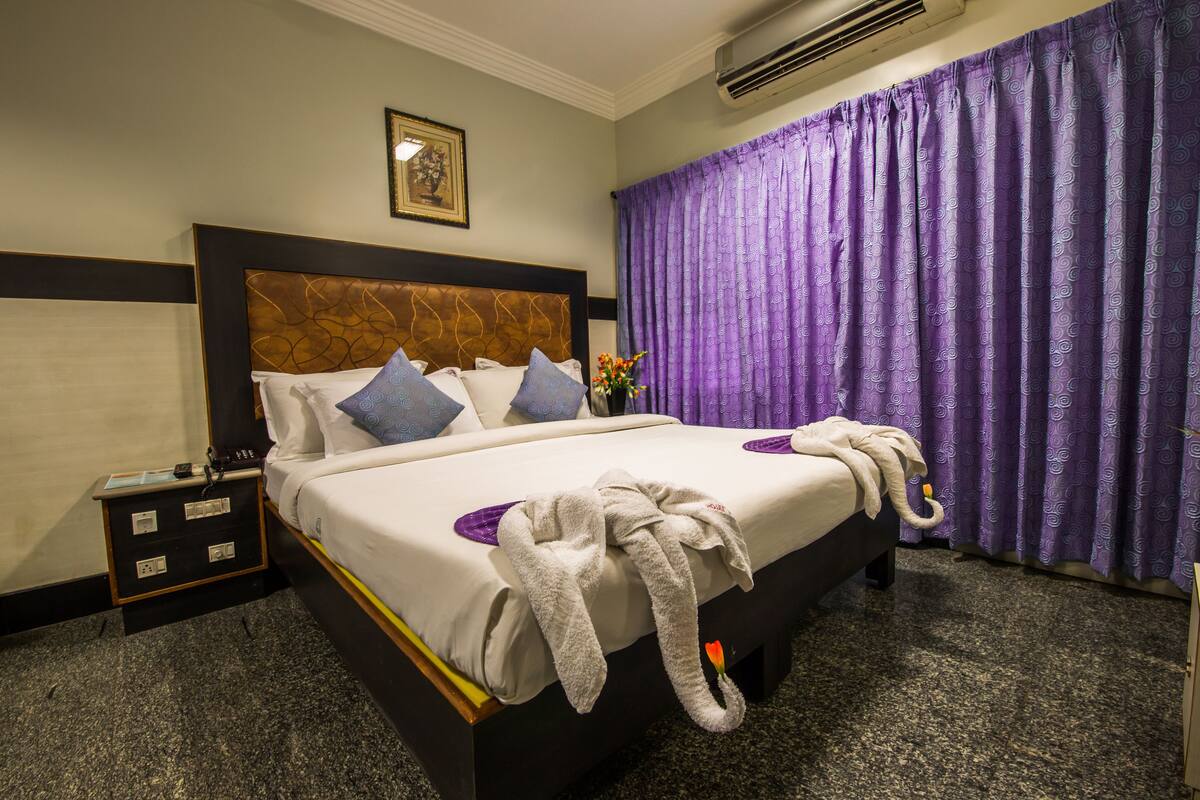 A hotel room with a bed, a nightstand, a telephone, and a window with purple curtains.