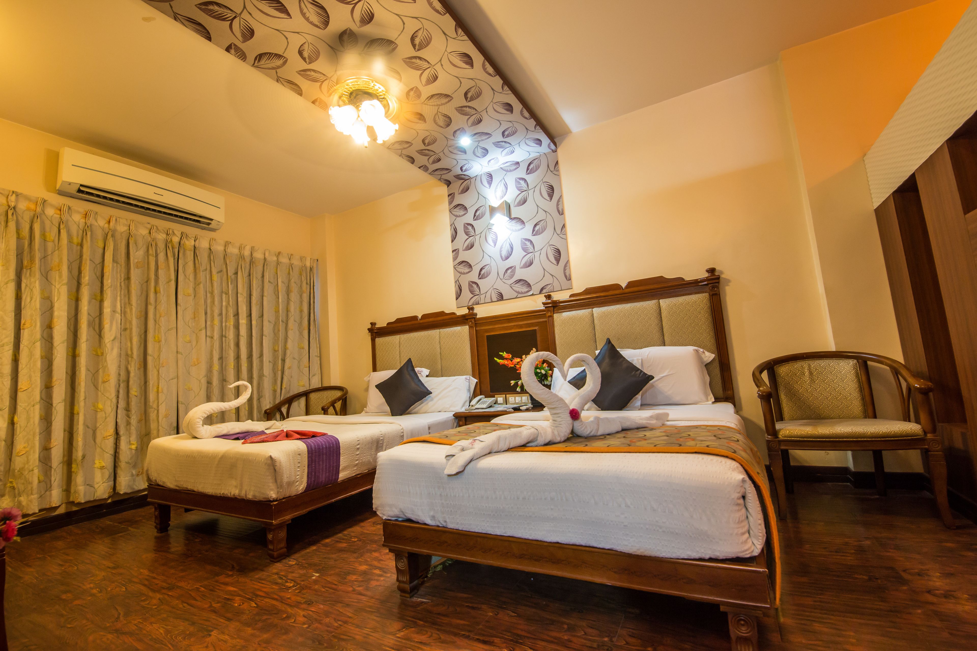 A hotel room with two beds, a wooden headboard, a chair, and a ceiling with a leaf pattern.