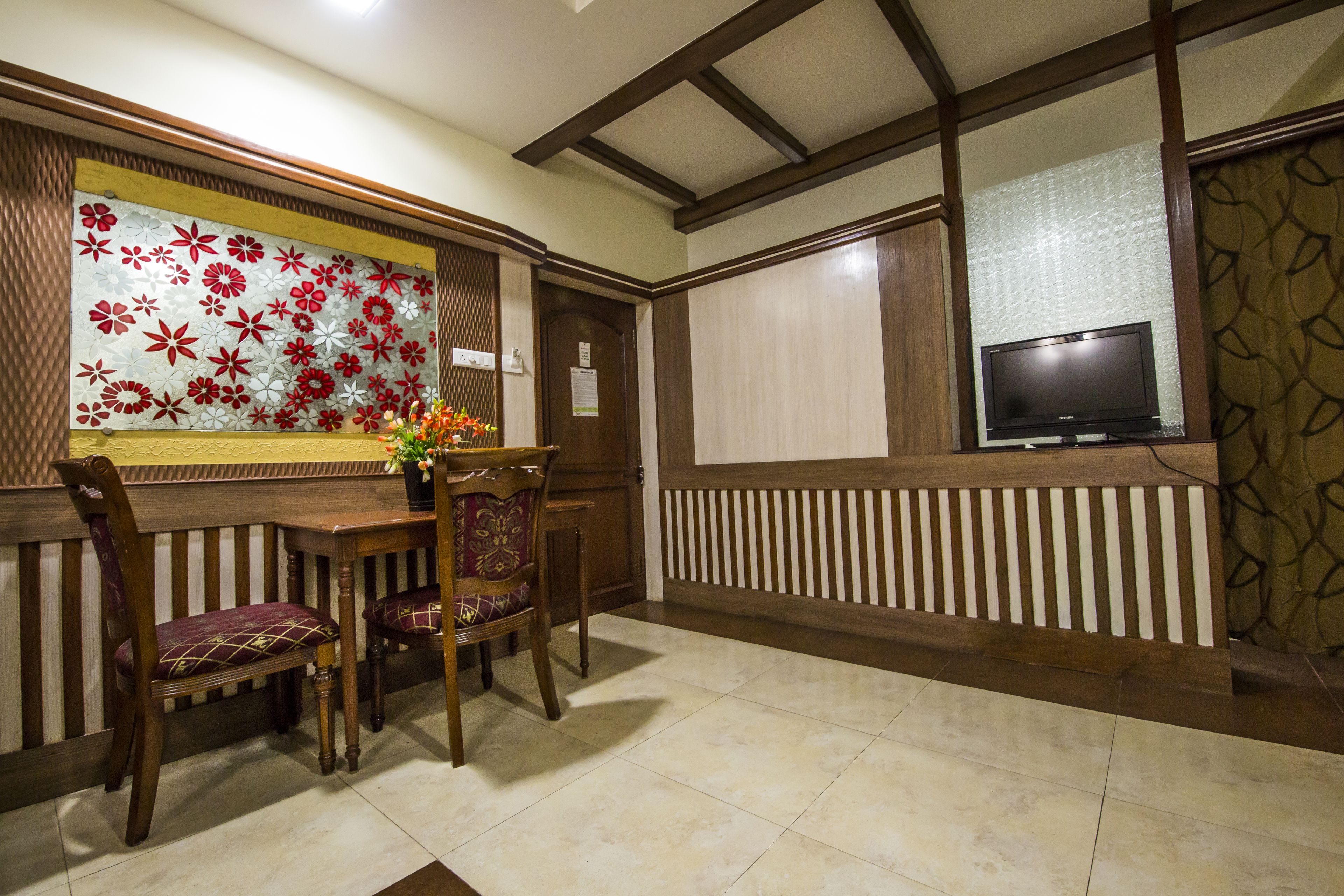 A dining area with wooden furniture, a television mounted on the wall, and decorative floral wallpaper.