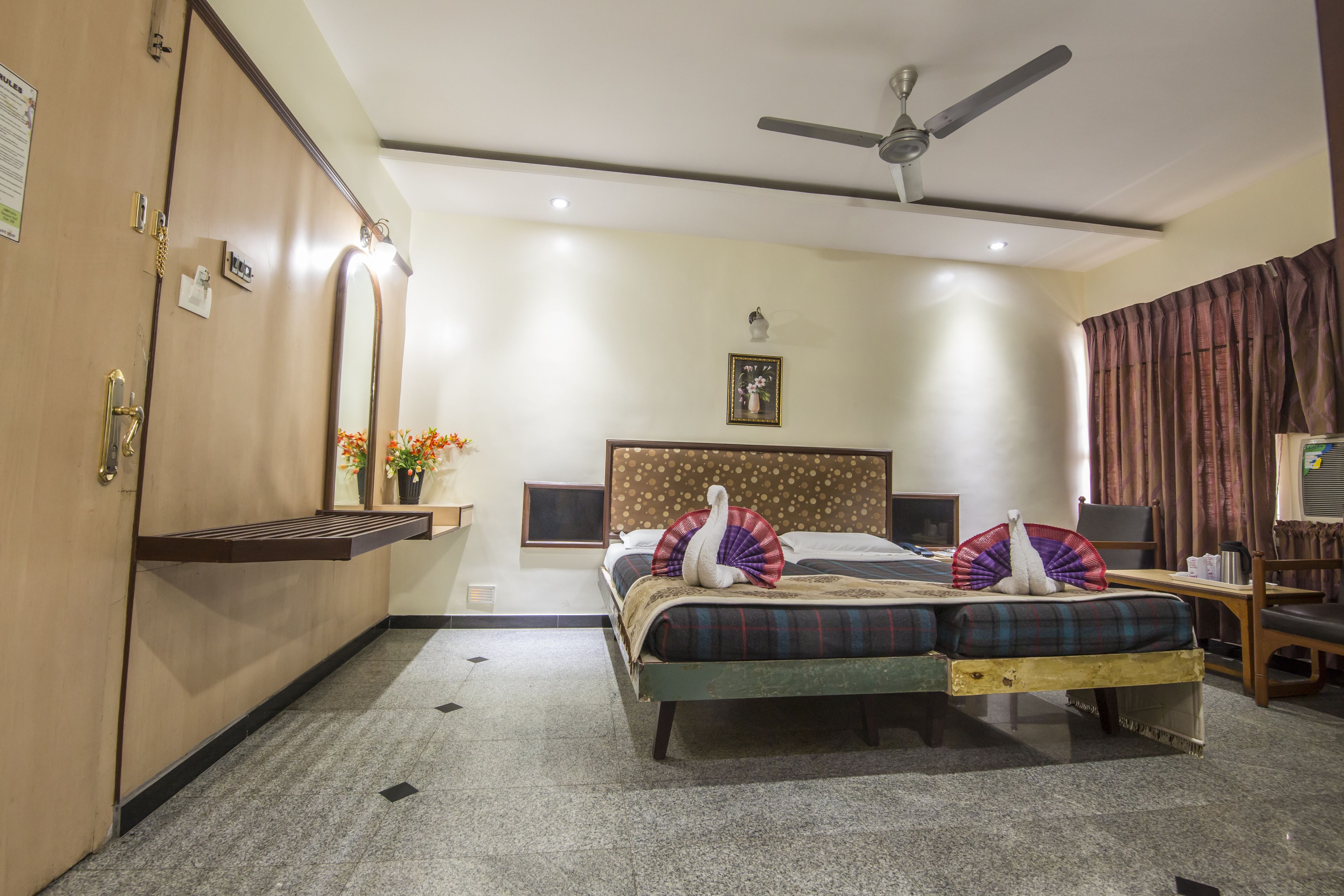 A hotel room with a bed, a ceiling fan, a nightstand, a TV, and a window with curtains.