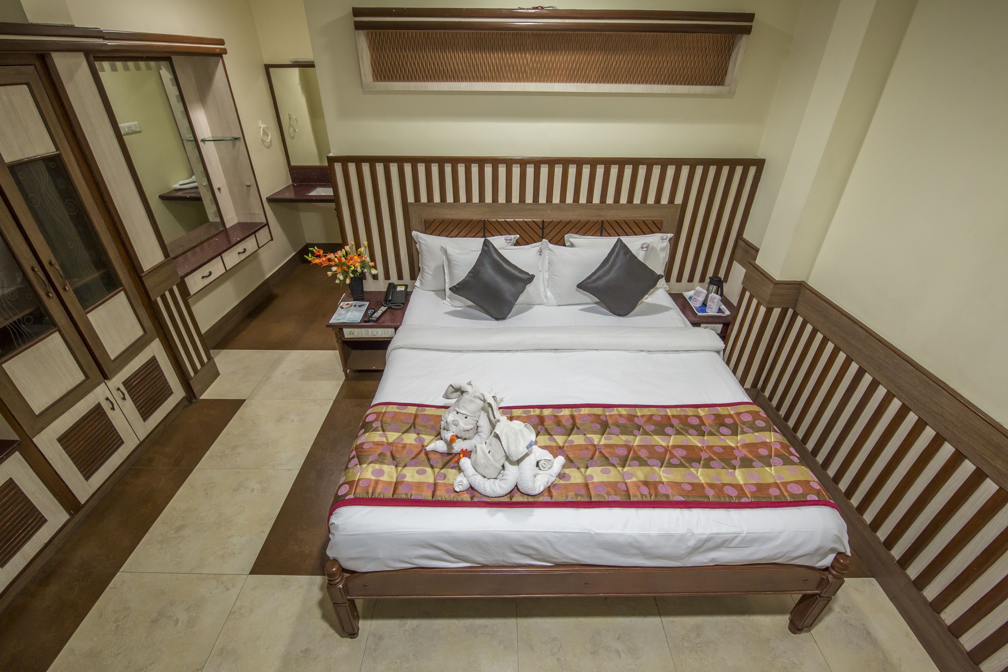 A neatly made bed with a patterned bedspread, a nightstand with a phone and a lamp, and a wardrobe with a mirror.