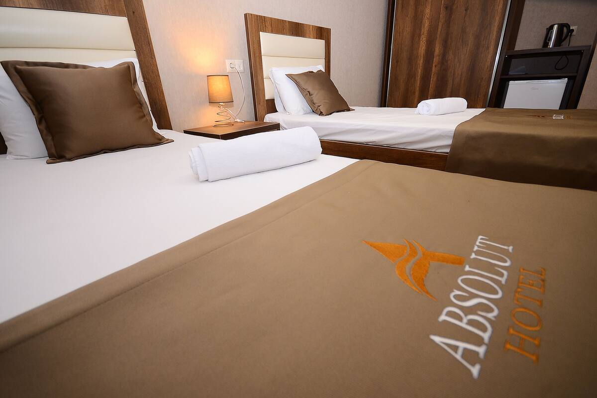 A hotel room with two beds, a nightstand with a lamp, and a minibar.