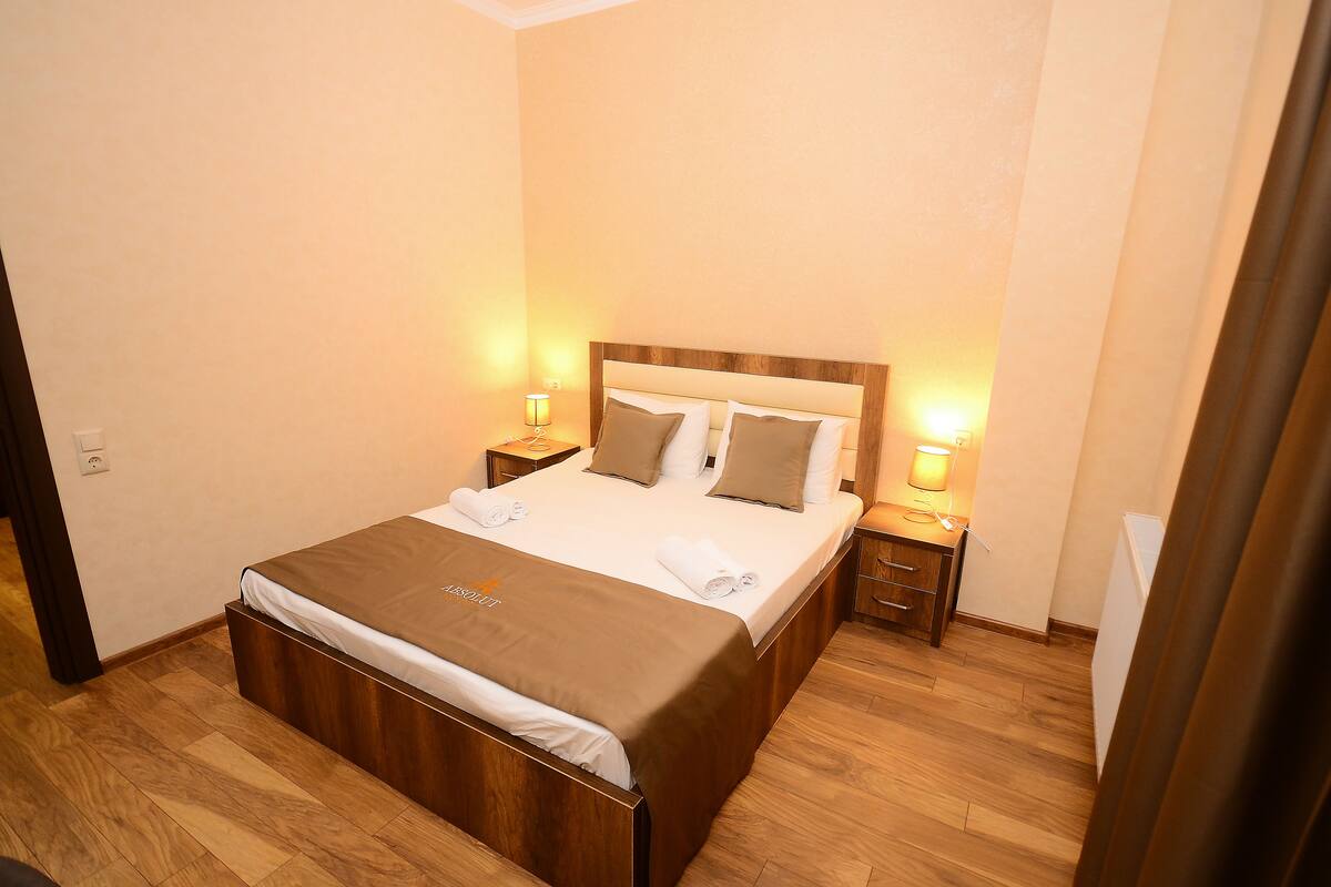 A neatly made bed with a brown headboard, two bedside tables with lamps, and a wooden floor.