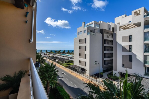 Un edificio moderno de varios pisos con balcones, vistas claras al océano y un área de estacionamiento al frente.