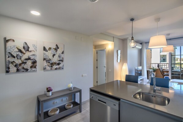 A modern kitchen with a built-in dishwasher, stainless steel sink, pendant lights, and artwork on the wall.