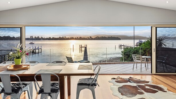 A dining area with a view of a lake, a wooden table, and chairs. - Peaceful Waterfront house Great View Private Jetty (Gosford)