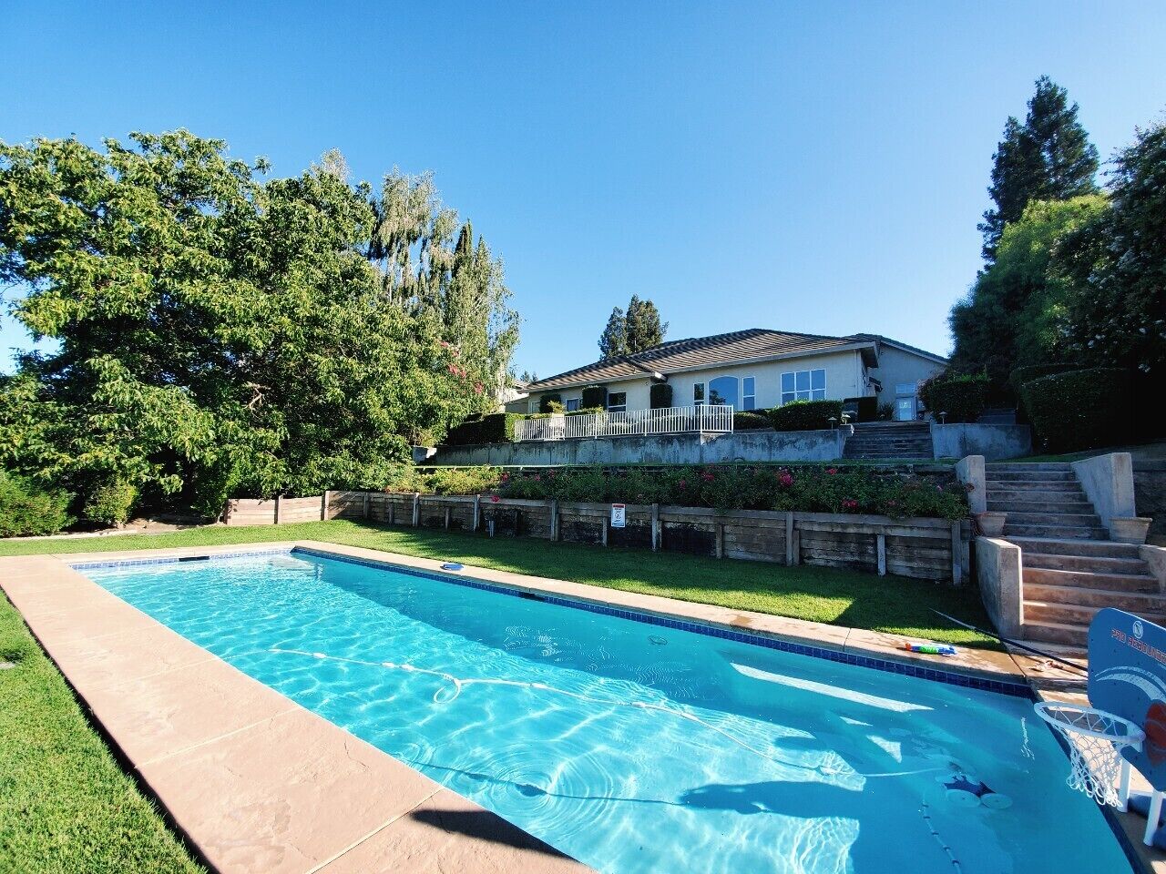 A rectangular swimming pool with clear blue water, surrounded by a grassy area and a stone wall.