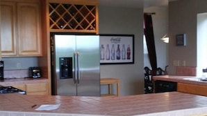 A kitchen with wooden cabinets, a stainless steel refrigerator, a bar area with stools, and a wall-mounted Coca-Cola sign. - Sip, Swim, Sleep Soak,Escape! Lodi wineries minutes away (Lockeford)