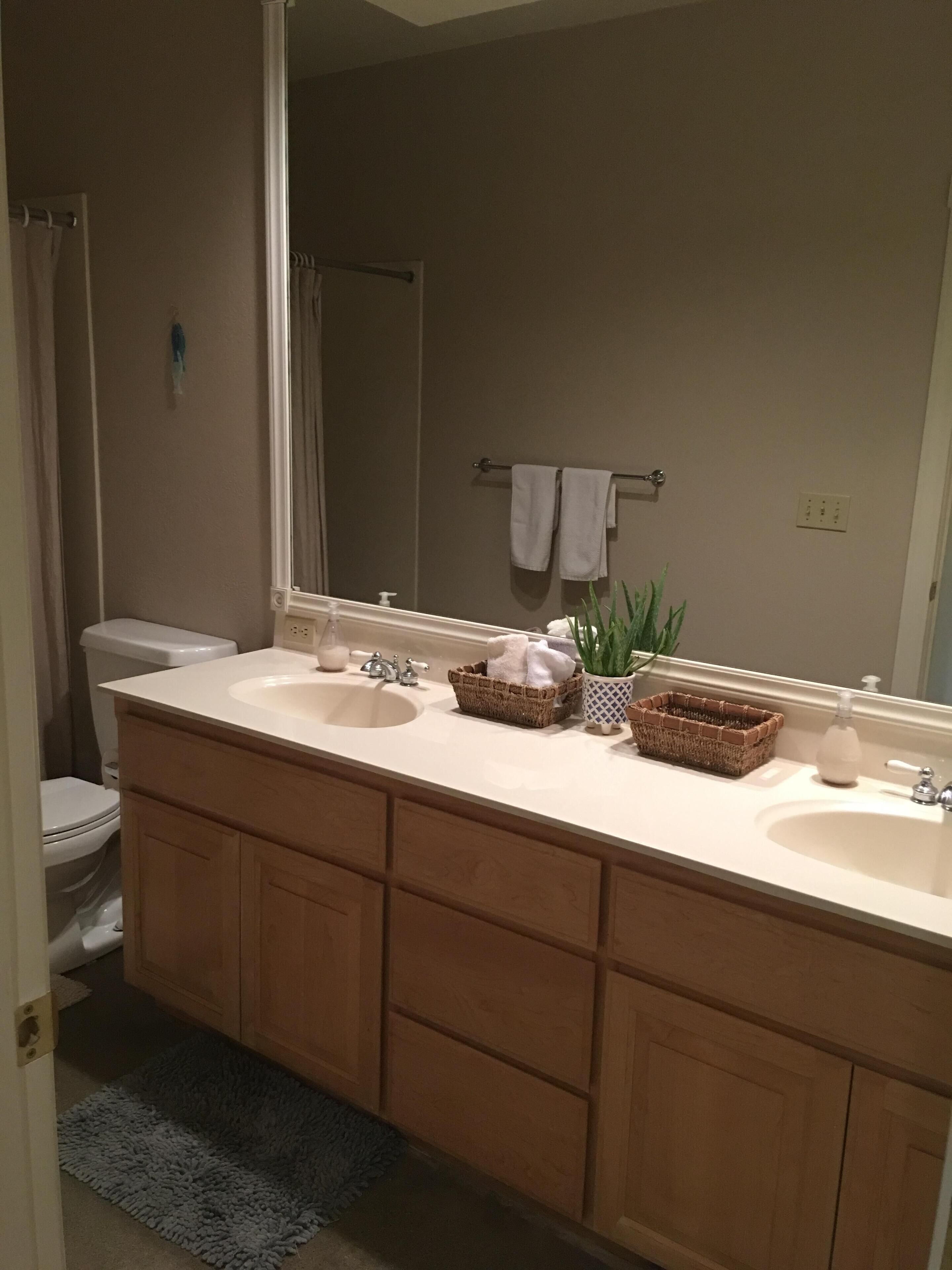 A bathroom with a double sink vanity, a mirror, a towel rack, and a toilet.