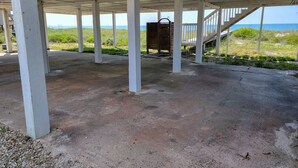 Un espacio exterior cubierto con piso de concreto y pilares blancos, que conduce a una escalera y ofrece vista al océano.