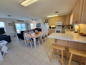 A modern kitchen with a central island, white cabinetry, and a dining area with white chairs.