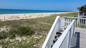 Vista de la playa con una terraza de madera y barandilla blanca.
