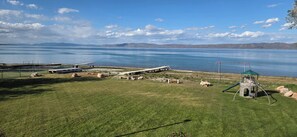 A grassy area with a playground, a small bridge, and a body of water with mountains in the background.