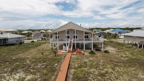 A two-story house with a covered porch and a small deck, surrounded by open fields and other houses. - YOU WILL INDEED be on Cloud Nine when you stay in this beautiful, beachfront home. (St. George Island)