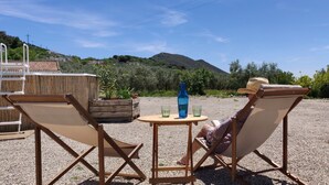 Zwei Liegestühle blicken auf einen Tisch mit einer Flasche und Gläsern, platziert auf einer Schotterfläche mit Blick auf Berge.