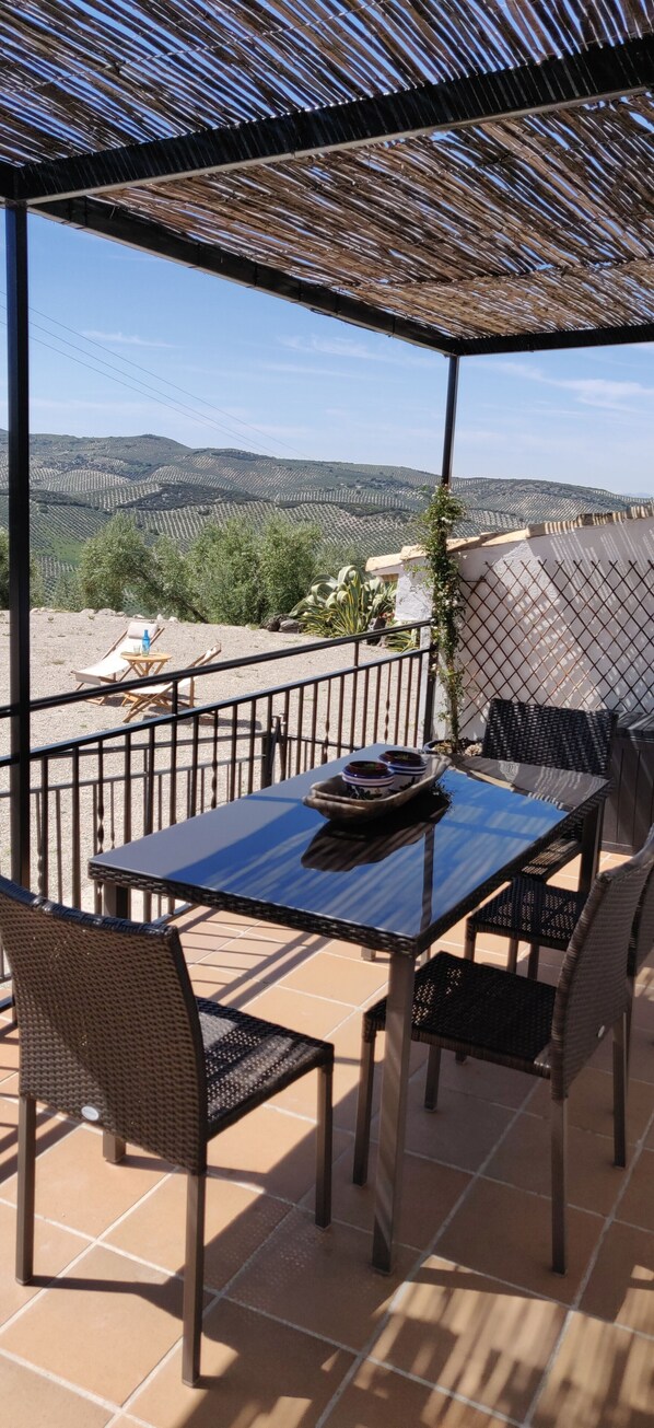 Un patio exterior con una mesa y sillas, una pérgola y vistas a colinas distantes.