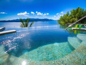 Una piscina infinita con agua cristalina, una palmera y una vista de montaña al fondo.