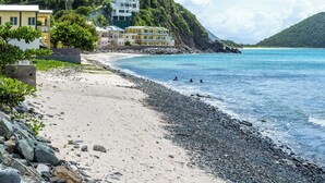 Una playa con costa rocosa, edificios en una colina y agua azul cristalina.
