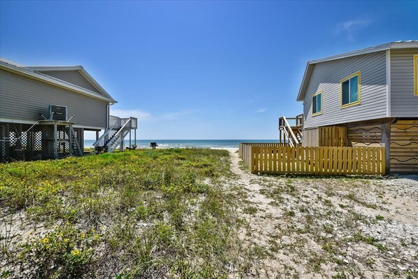 A beachfront property with two wooden houses, each with a porch and a staircase leading to a deck.