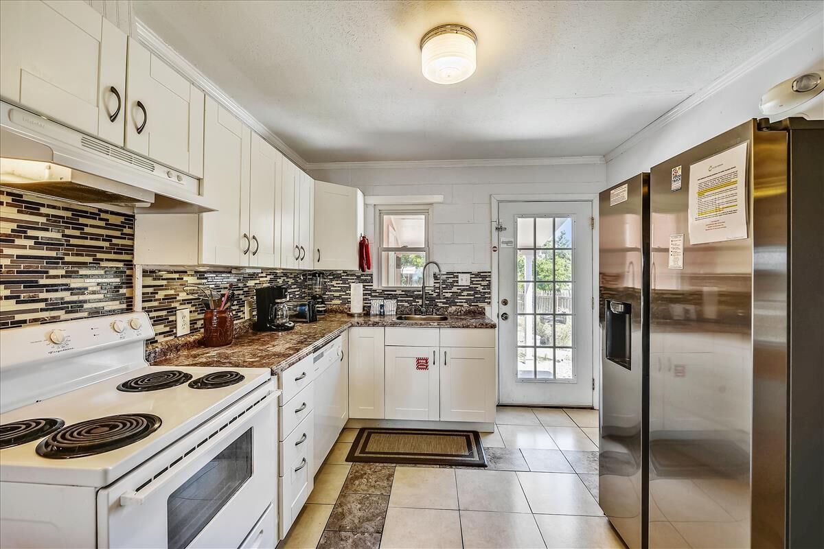 A modern kitchen with white cabinets, a built-in stove, a refrigerator, and a tiled backsplash.