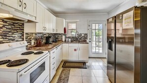 A modern kitchen with white cabinets, a built-in stove, a refrigerator, and a tiled backsplash. - Cozy Cabanas East. A newly renovated ground level duplex. (St. George Island)