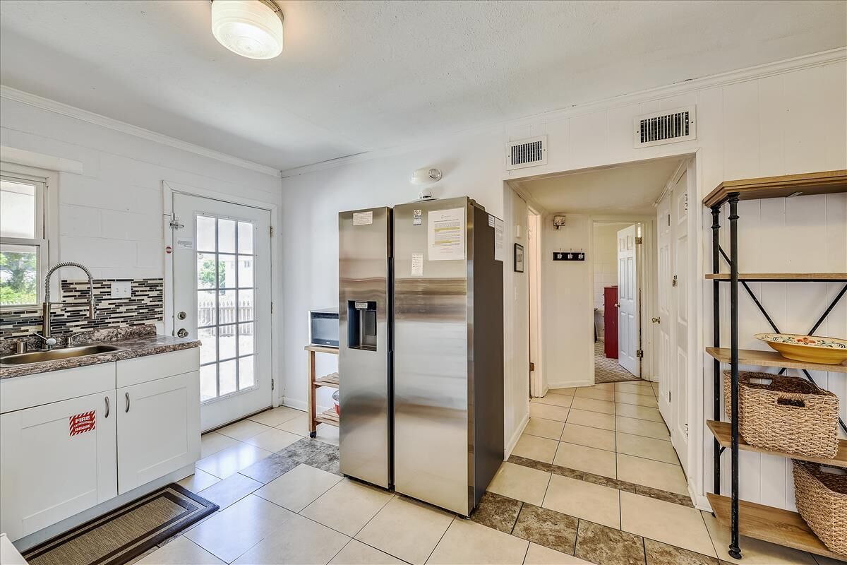A kitchen with white cabinets, a stainless steel refrigerator, a sink, and a window.