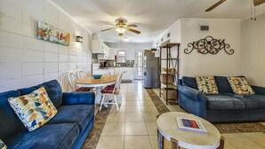 A modern living room with a blue sofa, a coffee table, and a dining area with a wooden table and chairs. - Cozy Cabanas East. A newly renovated ground level duplex. (St. George Island)