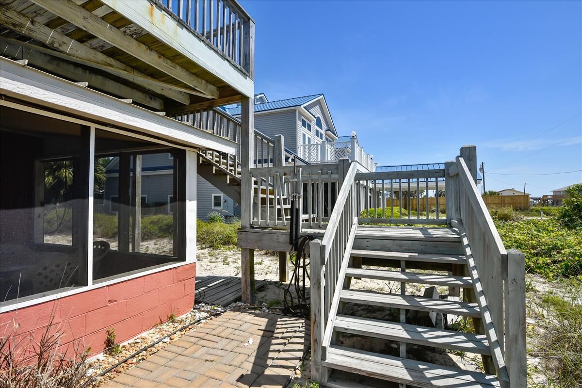 A coastal house with a wooden deck and a staircase leading to a balcony.